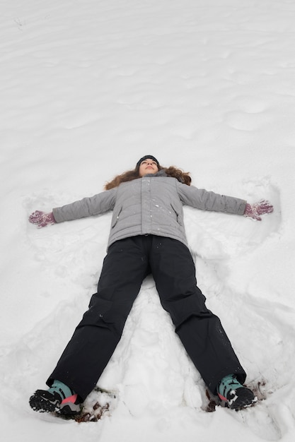 Vista dall'alto di una ragazza che gioca nella neve indossando vestiti caldi