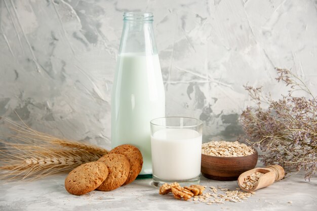 Top view of glass bottle and cup filled with milk on wooden tray and cookies spoon oats in brown pot spike on white table on ice background