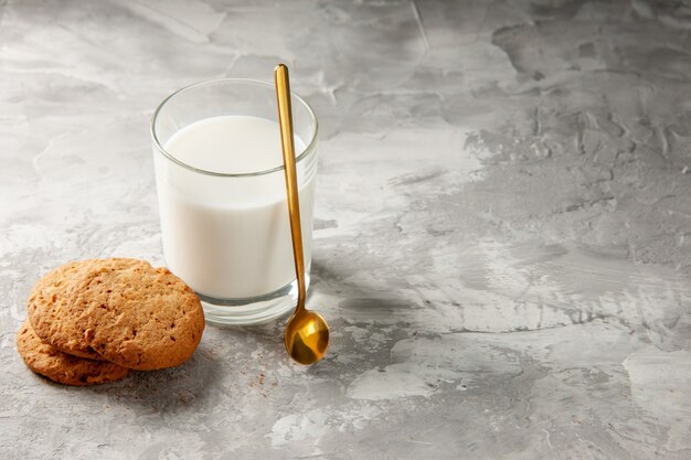 空きスペースのある灰色のテーブルの右側にミルクと金のスプーンクッキーで満たされたガラスカップの上面図