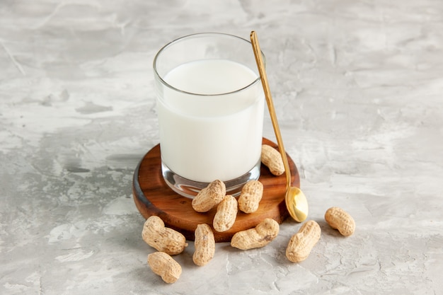 Top view of glass cup filled with milk on wooden tray and dry fruits spoon on white surface
