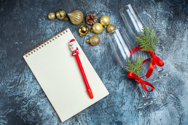 Top view of glass goblets with red ribbon and decoration accessories notebook with pen on dark background