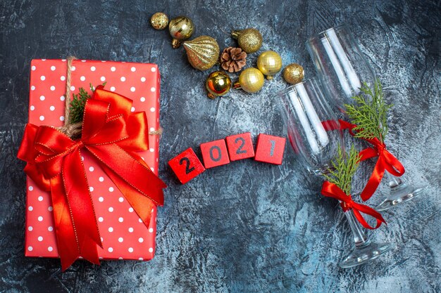 Top view of glass goblets with red ribbon and numbers decoration accessories next to gift boxes on dark table