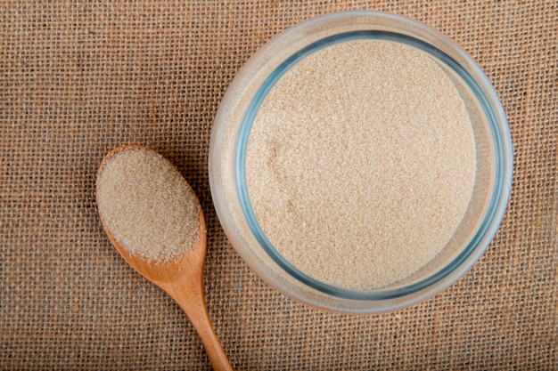 Top view of a glass jar filled with granulated brown sugar on sackcloth texture background