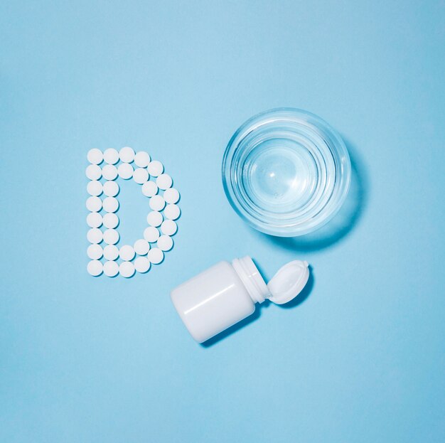 Top view of glass of water and container with pills spelling letter d