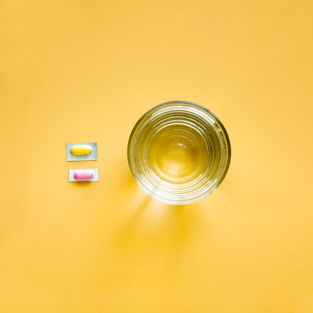 Вид сверху стакан воды и таблетки в фольге
