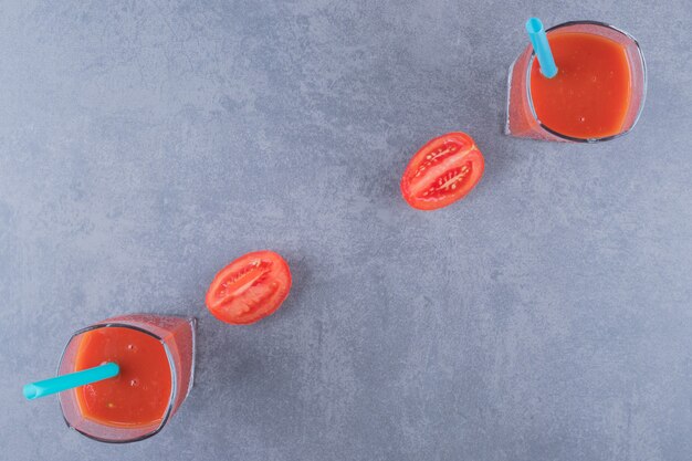 top view of glasses of fresh tomato juice and tomatoes on a grey background.