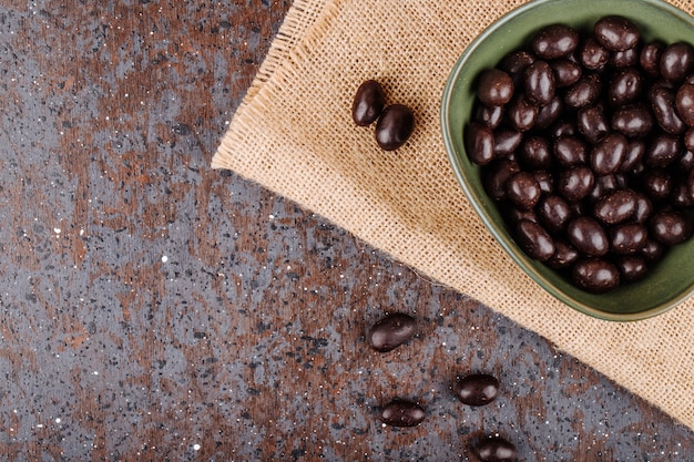 Vista superiore della caramella glassata del dado del cioccolato in una ciotola su tela di sacco su fondo rustico con lo spazio della copia