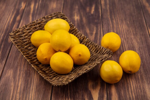 Вид сверху хорошего источника витамина c лимоны на плетеном подносе с лимонами, изолированными на деревянной поверхности