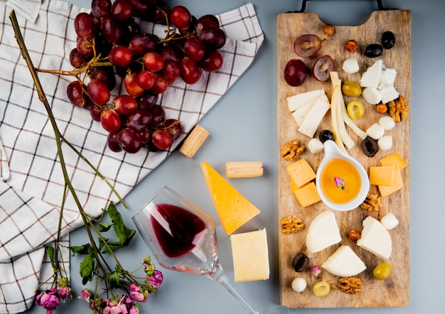 Top view of grape and flowers on cloth with cheese olive nuts butter on cutting board and glass of wine corks on white