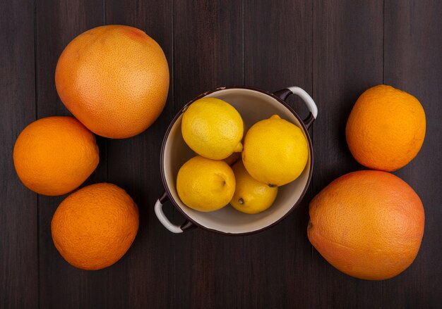 Top view grapefruit with oranges and lemons in a saucepan on wood background