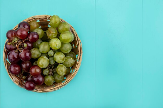 Top view of grapes in basket on blue background with copy space