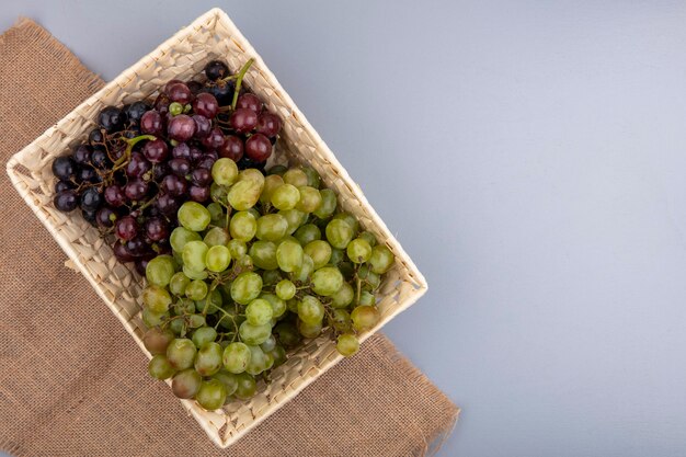 Top view of grapes in basket on sackcloth on gray background with copy space