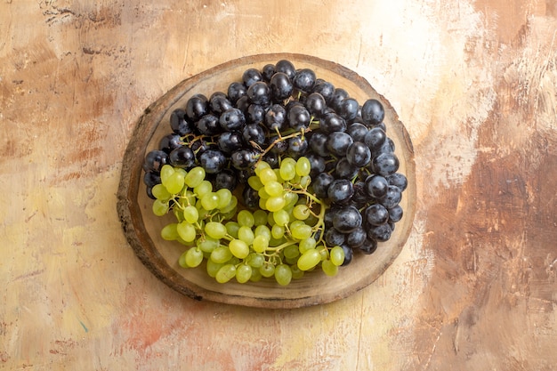 Вид сверху гроздей зеленого и черного винограда на кухонной доске