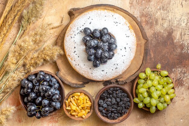 Top view of grapes a cake with grapes on the board bowls of raisins grapes spikelets