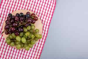Foto gratuita vista dall'alto di uva sul tagliere su panno plaid e su sfondo grigio con spazio di copia