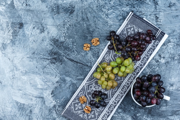 Бесплатное фото Вид сверху виноград в белой чашке с грецкими орехами на гранж и фоне кухонного полотенца. горизонтальный