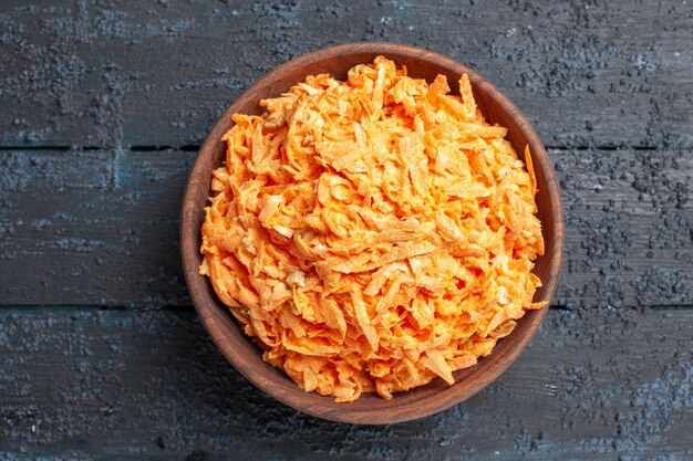 Вид сверху салат из тертой моркови внутри тарелки на темно-синем деревенском столе салат цвета спелых здоровых диетических овощей