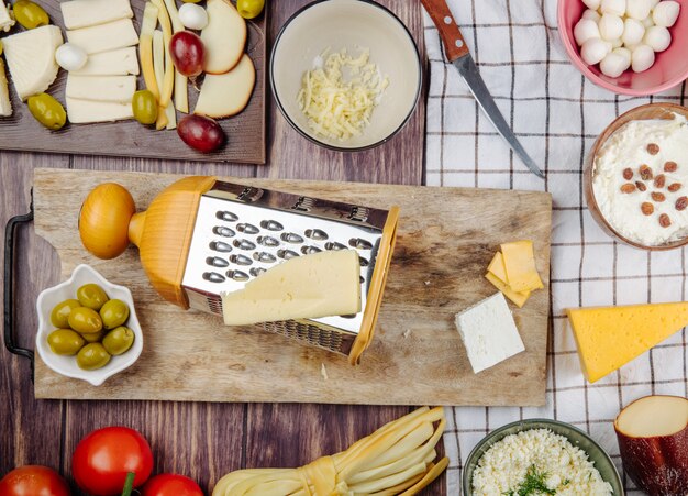 Top view of grater with cheese and pickled olives on a wood cutting board on rustic