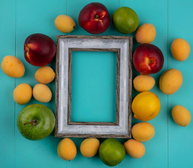 Top view of gray frame peaches apples apricots lemon and lime on a blue surface