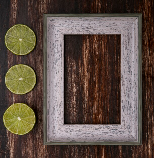 Top view of gray frame with lime slices on a wooden surface