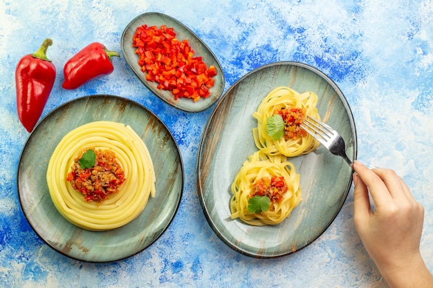 Foto gratuita vista dall'alto di un piatto grigio con deliziosi spaghetti e tenendo la pasta sul tavolo blu