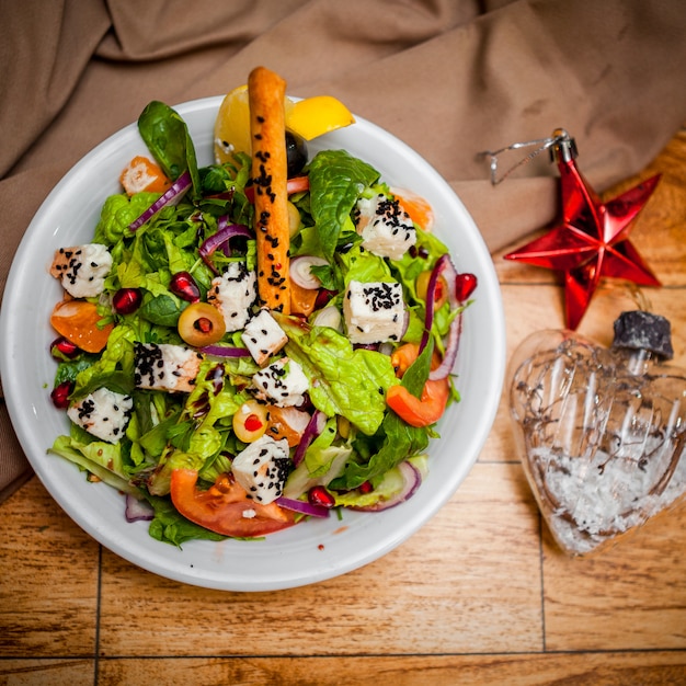 Top view greek salad with christmas toys in round white plate on table
