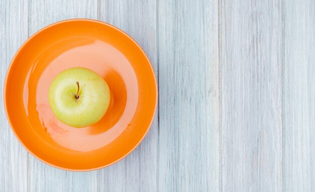Top view of green apple in plate on wooden background with copy space