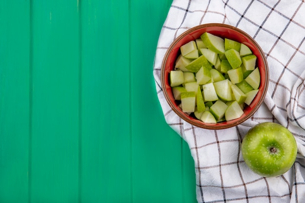 Top view of green apple with chopped slices on cloth on green surface