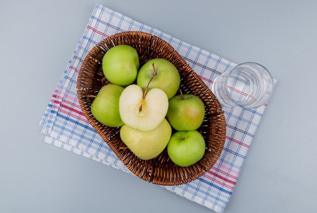Top view of green apples in basket and glass of water on plaid cloth and gray background