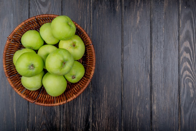 Top view of green apples in basket on wooden background with copy space