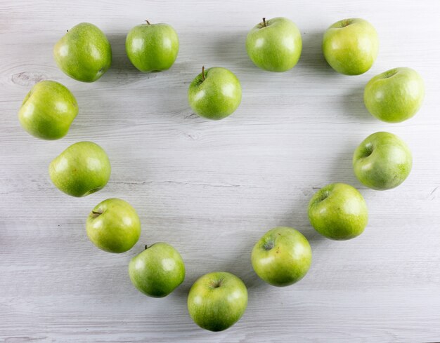 Top view green apples heart on white wooden  horizontal