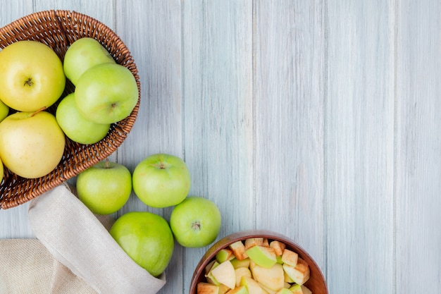 Free photo top view of green apples spilling out of sack and basket of apples with bowl of apple cubes on wooden table with copy space