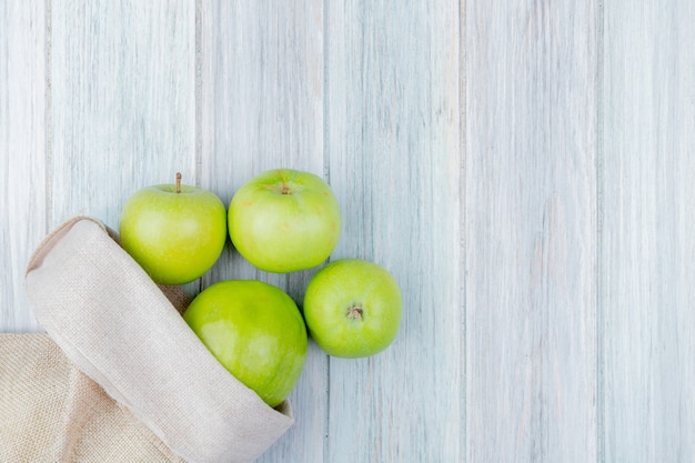 Top view of green apples spilling out of sack on wooden background with copy space