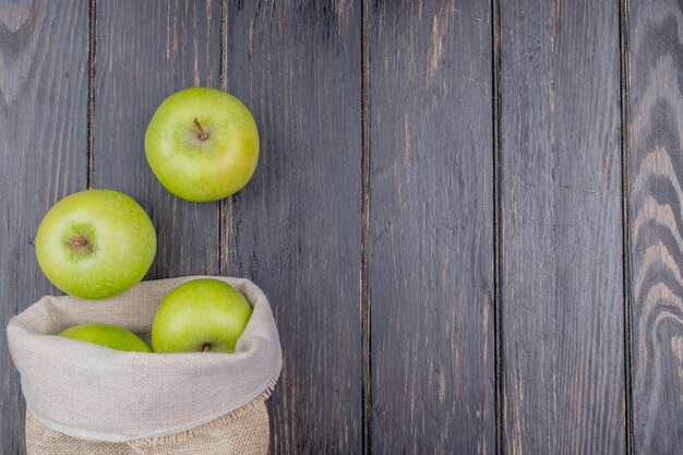 top view of green apples spilling out of sack on wooden background with copy space
