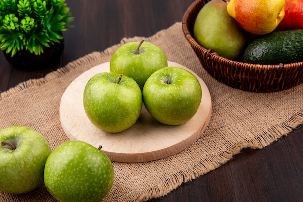 Top view of green apples on a wooden kitchen board on sack cloth on wooden surface