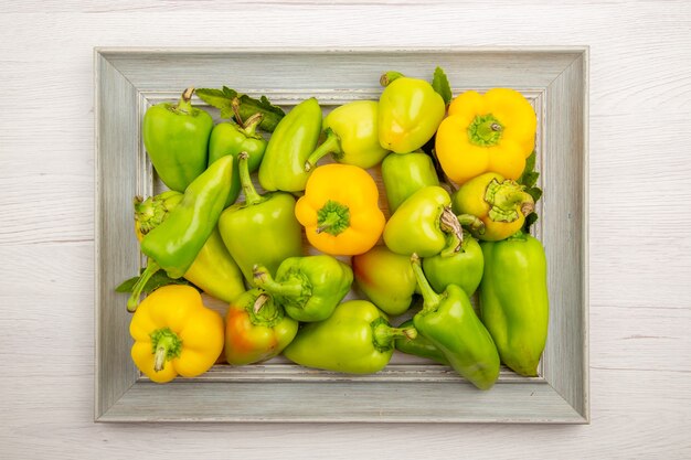 Top view green bell-peppers inside frame on white table