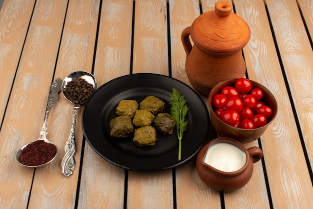 Foto gratuita vista dall'alto dolma verde all'interno della banda nera con yogurt e pomodori rossi sulla scrivania in legno