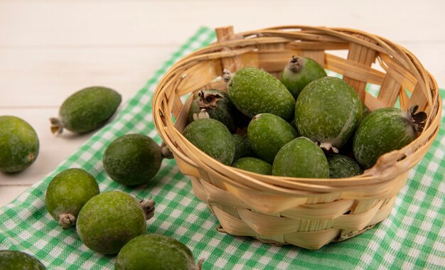 Top view of green feijoa on a bucket on a green checked cloth on a white wooden wall