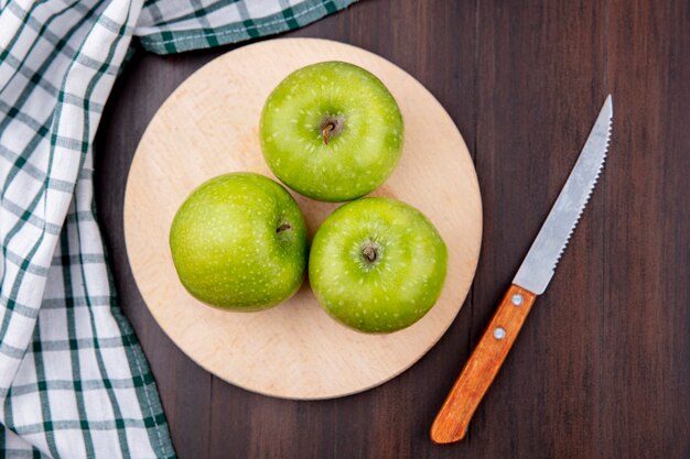 Top view of green and fresh apples on a wooden kitchen board with knife with checked cloth on wooden surface