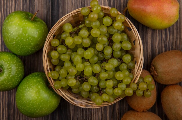 Top view green grapes in a basket with green apples and kiwi on a wooden background