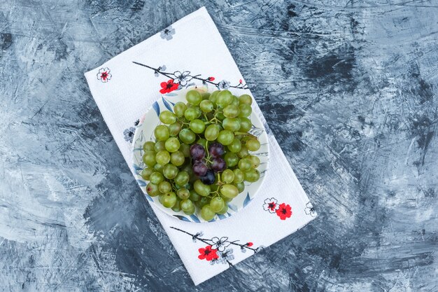 Top view green grapes in plate on grungy plaster and kitchen towel background. horizontal