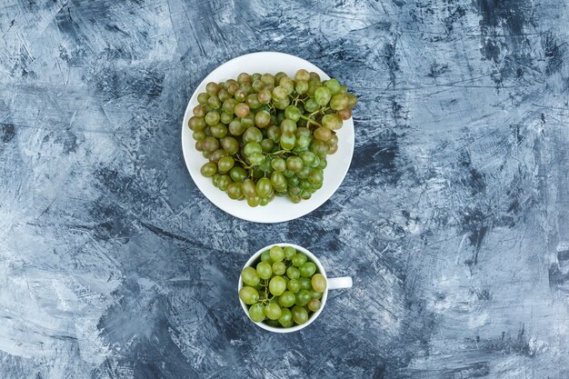 Top view green grapes in white plate and cup on grungy plaster background. horizontal