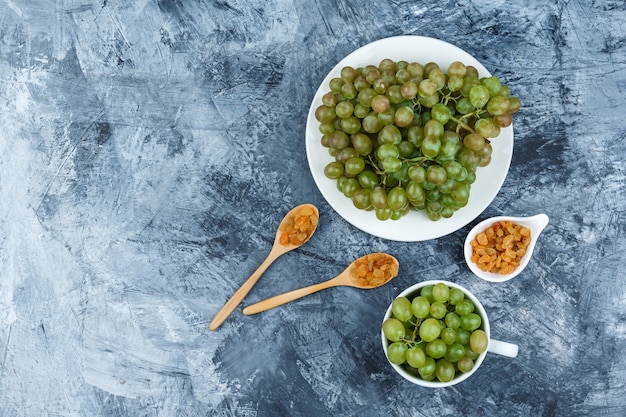 Top view green grapes in white plate and cup with raisins on grungy plaster background. horizontal