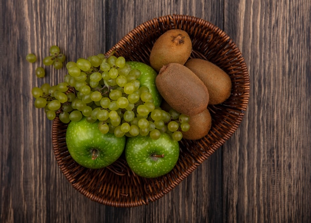 Top view green grapes with apples and kiwi in a basket on a wooden background