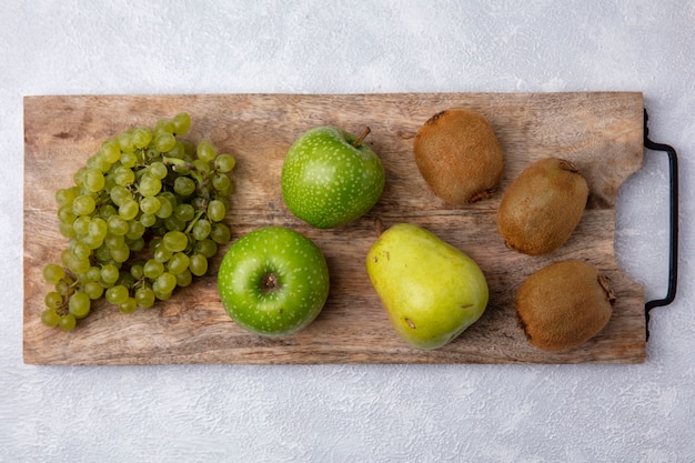 Vista dall'alto uva verde con mele verdi pera e kiwi su un supporto contro uno sfondo bianco