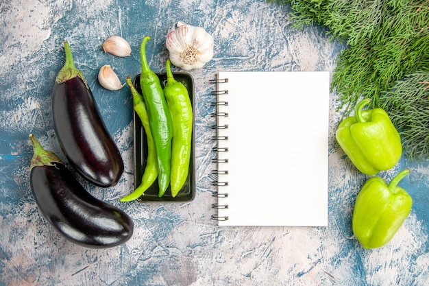 Free photo top view green hot peppers on black plate garlic aubergines peppers a notebook on blue-white background