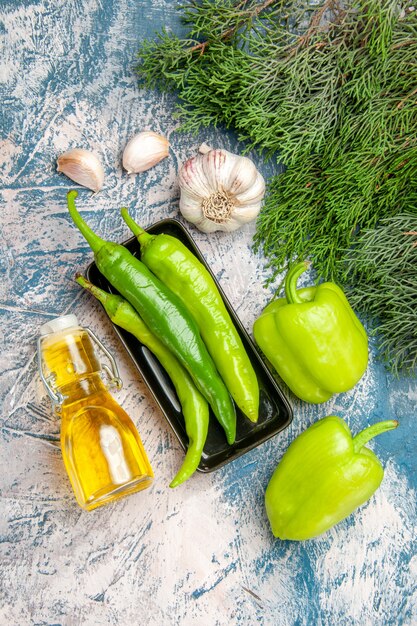 Top view green hot peppers on black plate garlic peppers bottle of oil on blue-white background