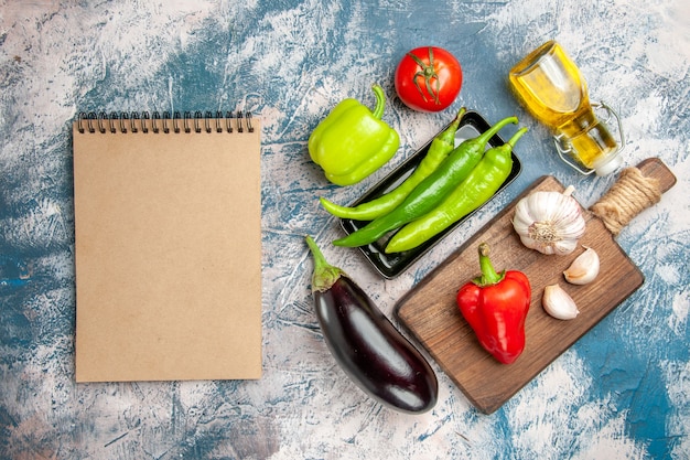 Top view green hot peppers on black plate tomato red and green peppers garlic on chopping board eggplant a notebook on blue-white background