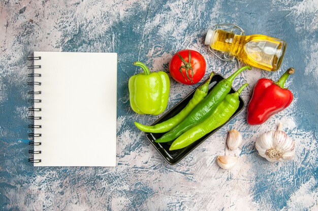 Top view green hot peppers on black plate tomato red and green peppers garlic a notebook on blue-white background