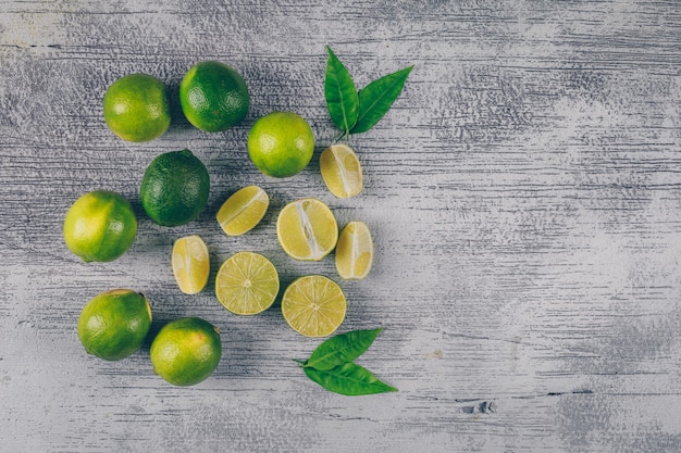 Top view green lemons with slices and leaves on gray wooden background. horizontal space for text